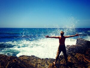 Man standing on rocks being splashed by ocean spray.