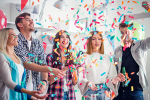 Office workers at a layoff party with balloons, confetti, and cupcakes.