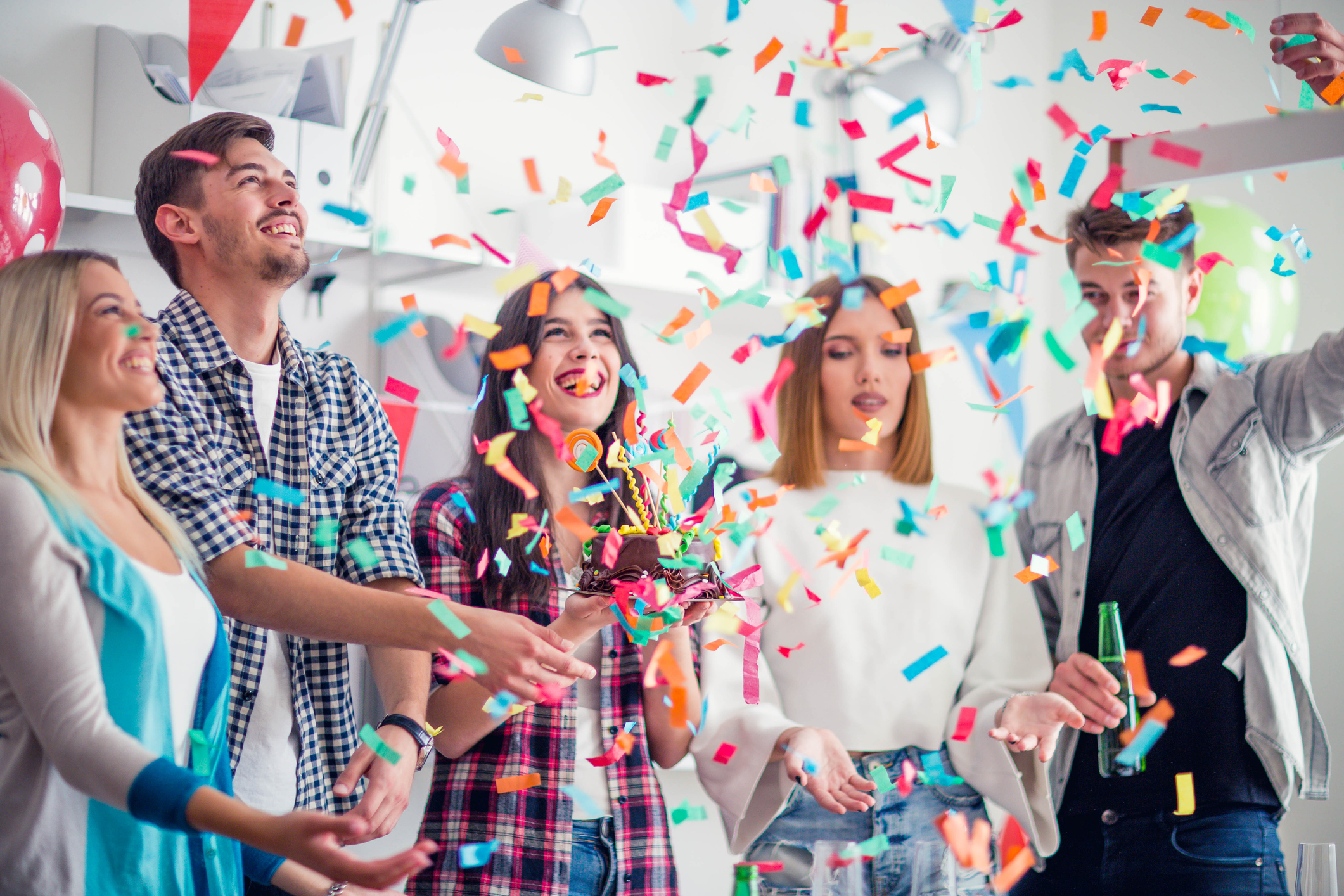 Office workers at a layoff party with balloons, confetti, and cupcakes.