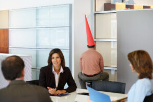 Office worker sitting in corporate detention with dunce cap on his head.