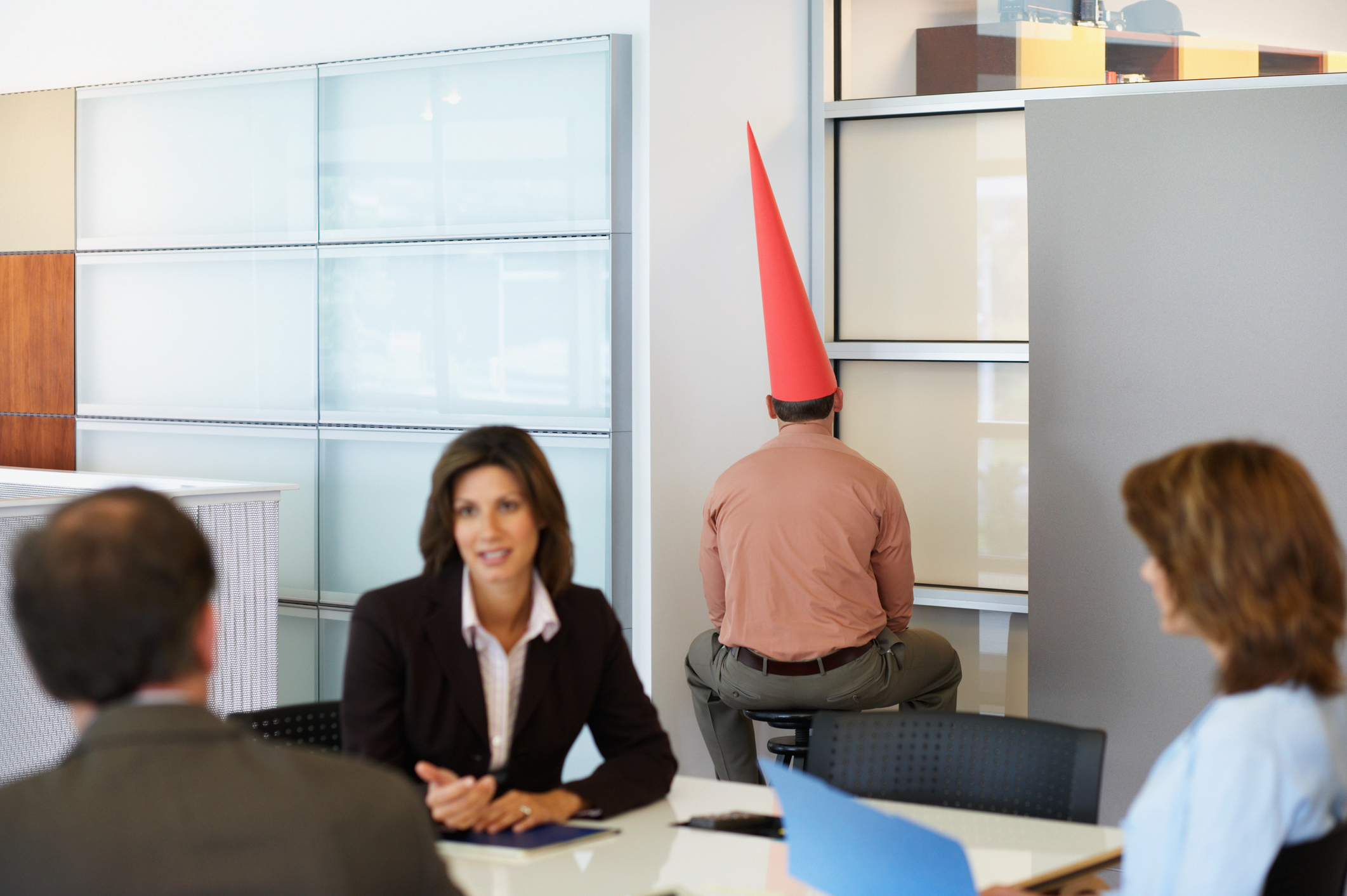 Office worker sitting in corporate detention with dunce cap on his head.