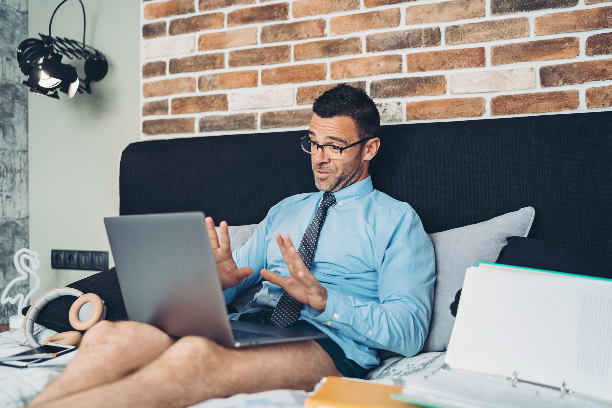 Man working from bed wearing a dress shirt and tie but no pants, perfectly capturing the chaos of mandatory camera-on corporate policies.
