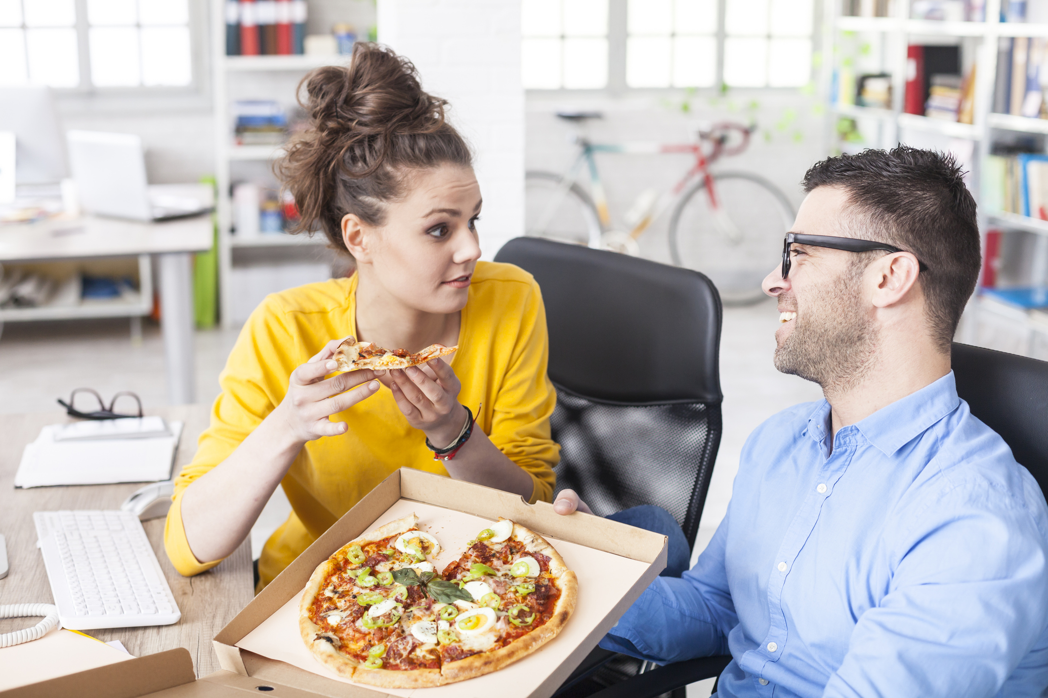Office workers in business attire eating pizza in the office.