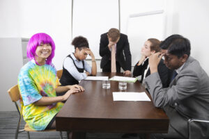 A tie-dye, pink-wigged employee beams as exhausted coworkers despair, highlighting a Culture Committee gone full shadow government.