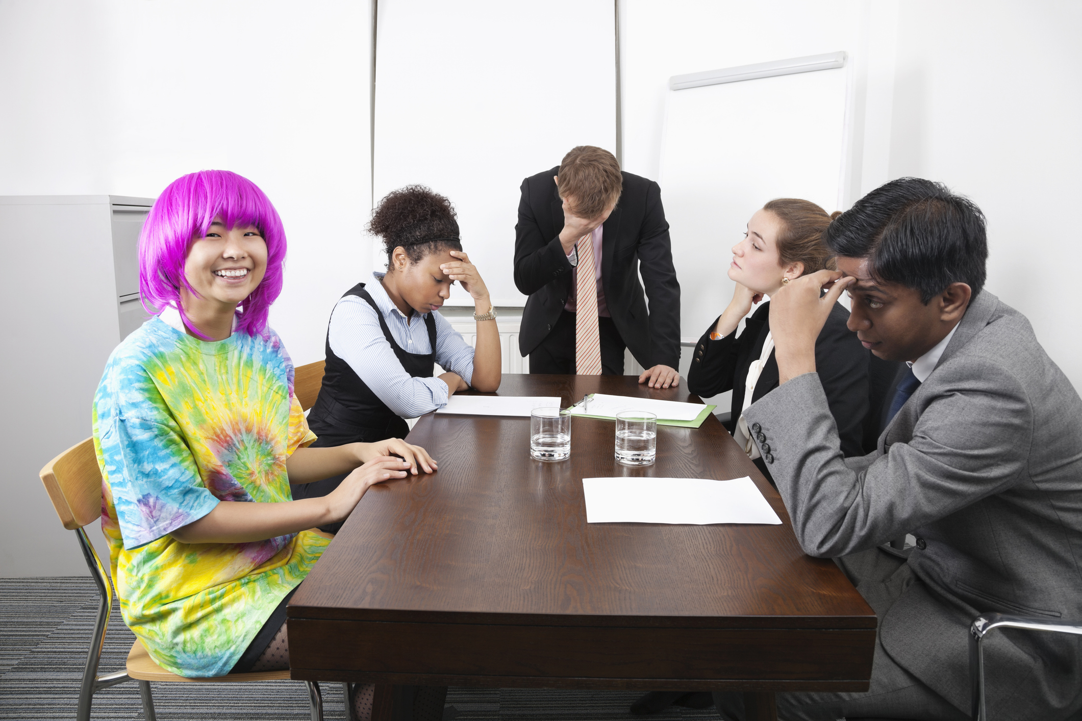 A tie-dye, pink-wigged employee beams as exhausted coworkers despair, highlighting a Culture Committee gone full shadow government.